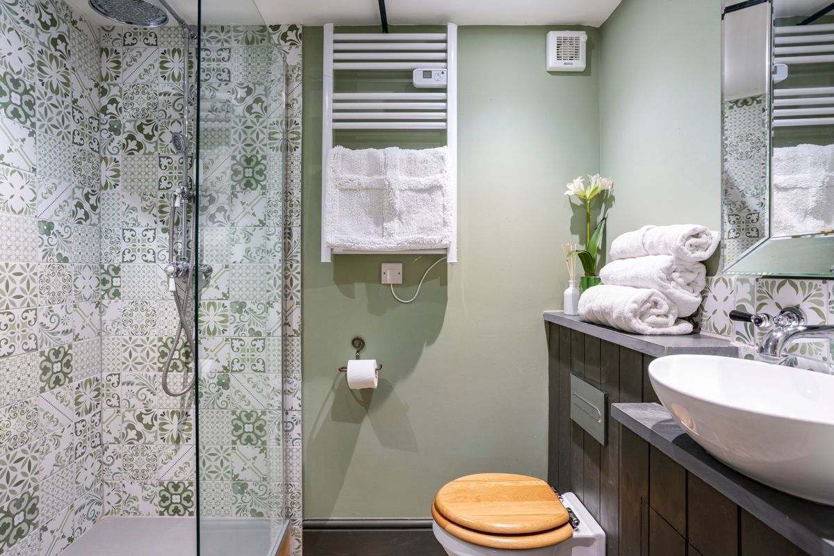 Une salle de bain avec des carreaux décorés, des toilettes en bois, un lavabo avec un miroir et un porte-serviettes.