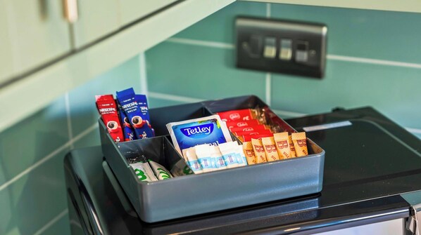Een dienblad met diverse verpakte etenswaren, waaronder een blauwe doos Tetley thee, rode en blauwe dozen met Nestle Original Decaf en verschillende chocoladerepen.
