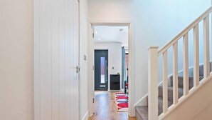 A hallway with a white door, a staircase with white railings, and a patterned rug on the floor. - New Central House | Contractor & Family Friendly (Reading)