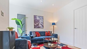A modern living room with a blue sofa, a glass coffee table, and a large plant. - New Central House | Contractor & Family Friendly (Reading)