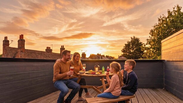 A group of people seated at a wooden table on a rooftop terrace with a sunset view. - New Central House | Contractor & Family Friendly (Reading)