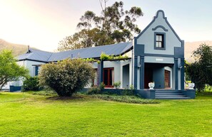 A two-story house with a gabled roof, a front porch, and a small garden area. - Oaksrest Vineyards Guest Farm (Ladismith)