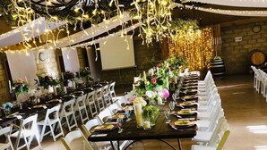 A banquet hall with long tables set for a formal event, white chairs, and string lights overhead. - Oaksrest Vineyards Guest Farm (Ladismith)