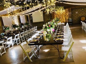 A banquet hall with long tables set for a formal event, white chairs, and string lights overhead. - Oaksrest Vineyards Guest Farm (Ladismith)