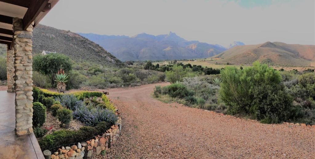 Un camino de grava que conduce a un edificio con fachada de piedra, rodeado de jardines cuidados y un telón de fondo montañoso.