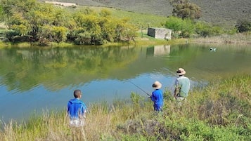 A calm lake with people fishing, surrounded by greenery and a stone structure.