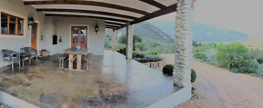 Un patio cubierto con mesa y sillas, pilares de piedra y vistas a un paisaje montañoso.