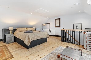Ein Schlafzimmer mit Bett, Nachttischen, Heizkörper, Holzboden und Blick ins Freie.