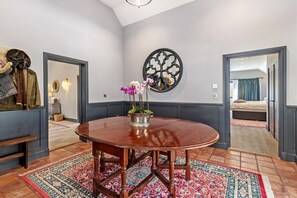 A dining area with a round wooden table, a patterned rug, and a wall-mounted decorative piece. - Cardigan Courtyard - Five Bedroom Villa, Sleeps 10 (Tan-y-groes)
