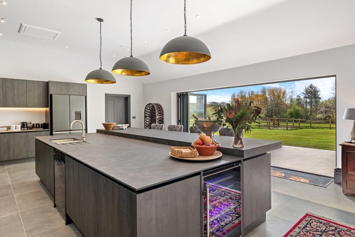 A modern kitchen with a large island, pendant lighting, and a view of the outdoors.