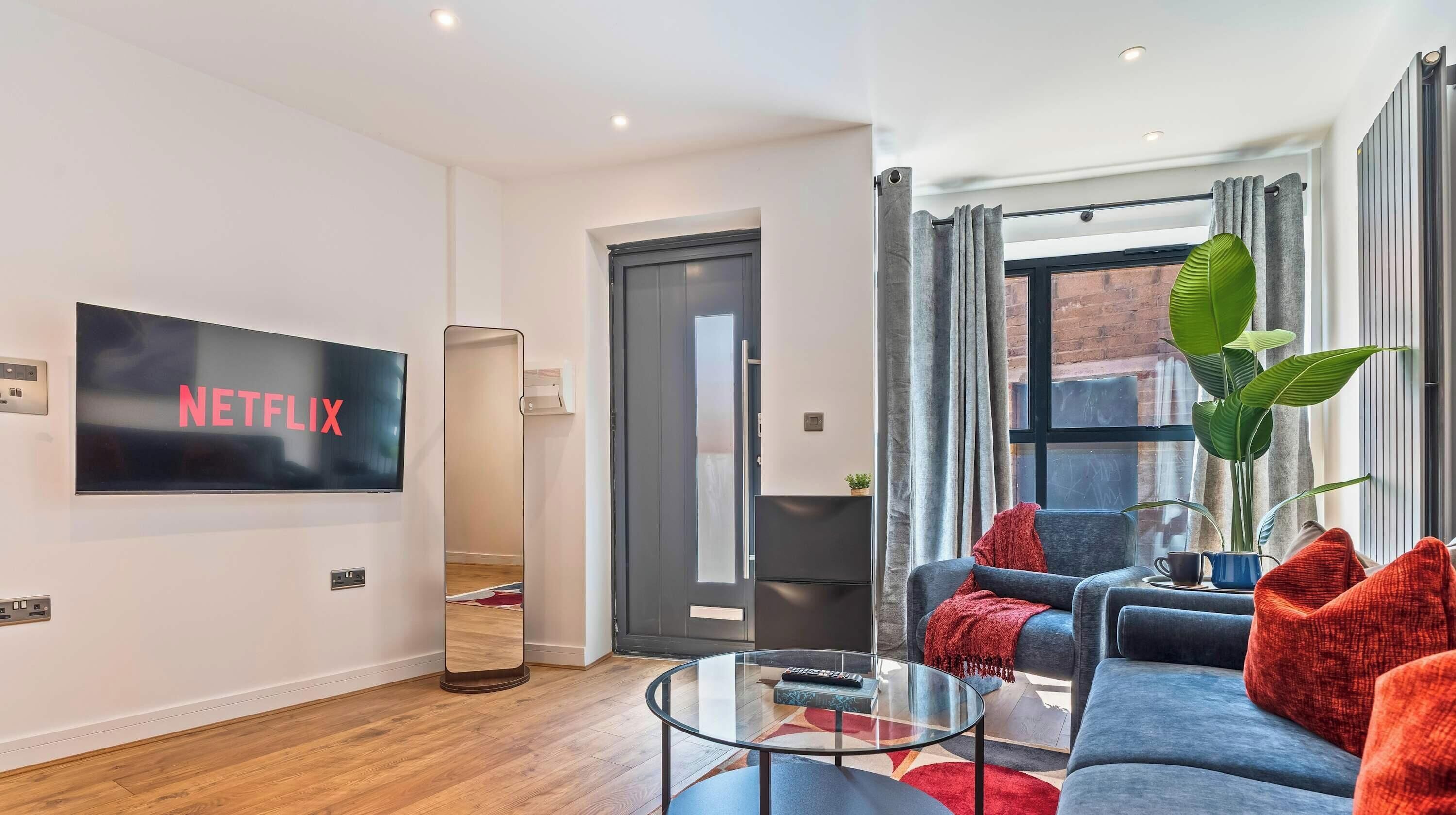 A modern living room with a flat-screen TV, a sofa, a coffee table, and a large window with curtains.