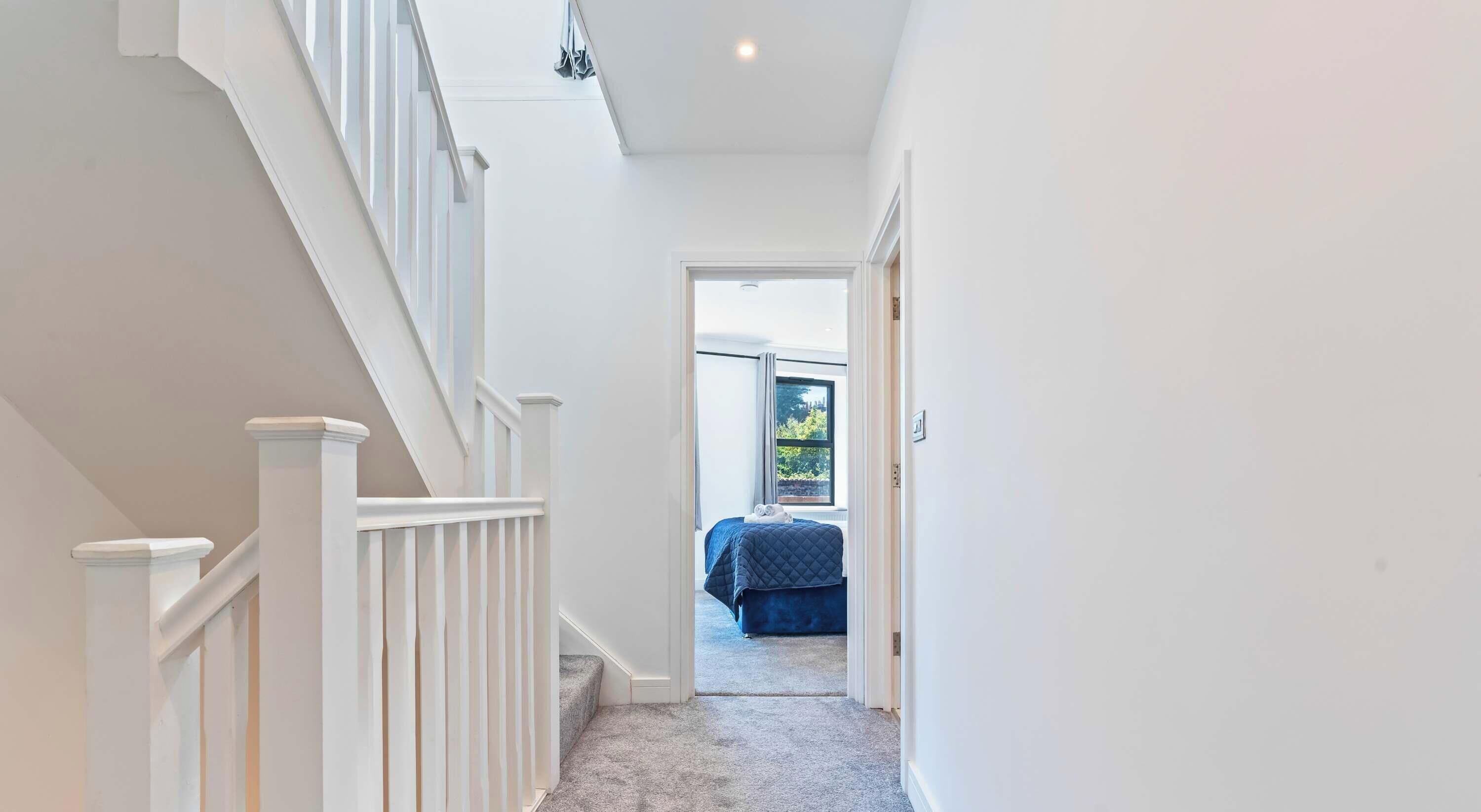 A hallway leading to a bedroom with a bed, a window, and a staircase.