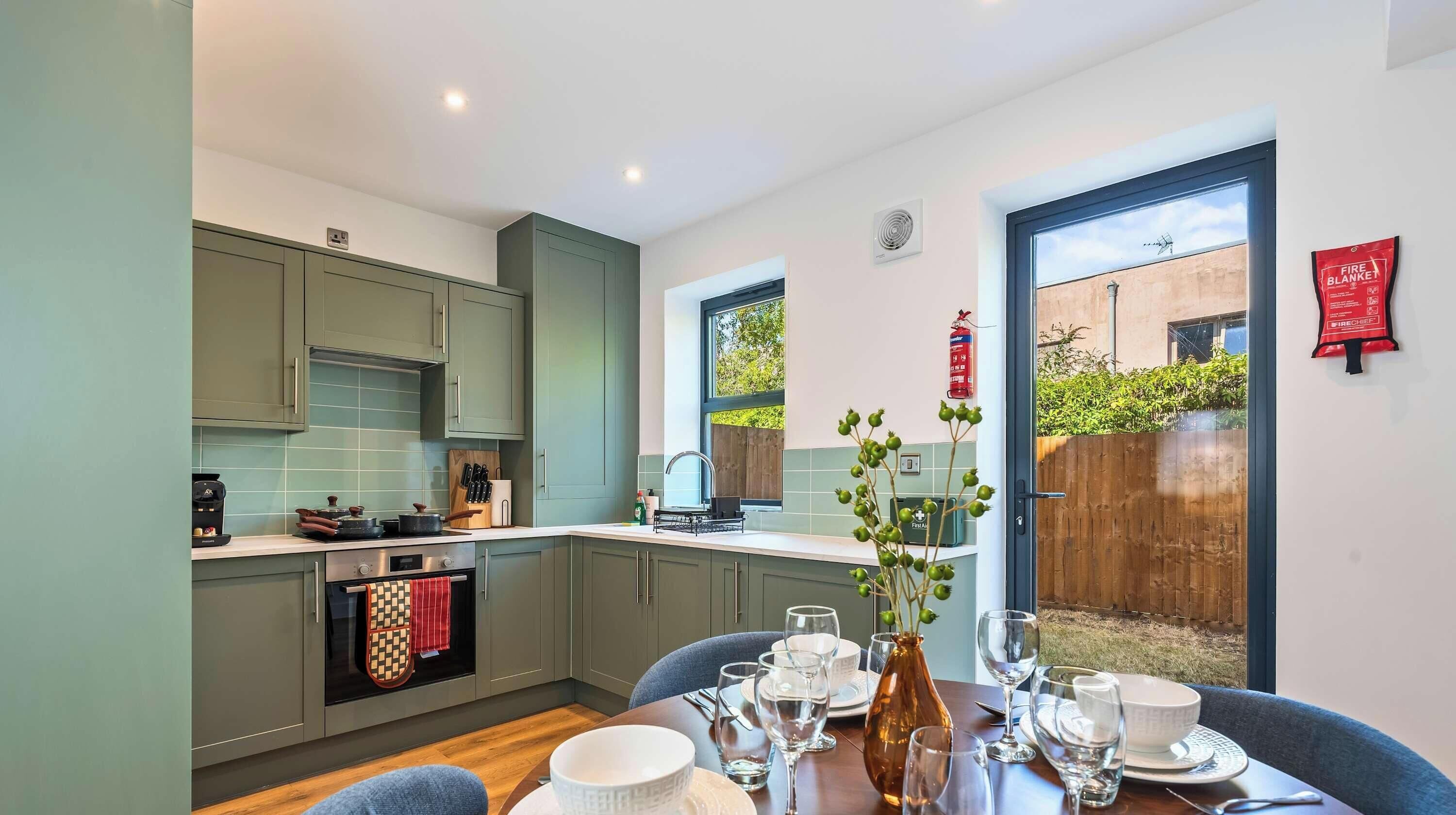 A modern kitchen with grey cabinets, a built-in oven, and a dining area with a table set for two.