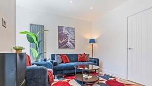 A modern living room with a blue sofa, a glass coffee table, and a large plant. - New Central Home | Groups, Contractor & Families (Reading)