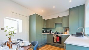 A modern kitchen with teal cabinets, a dining table set with glassware, and a coffee machine. - New Central Home | Groups, Contractor & Families (Reading)