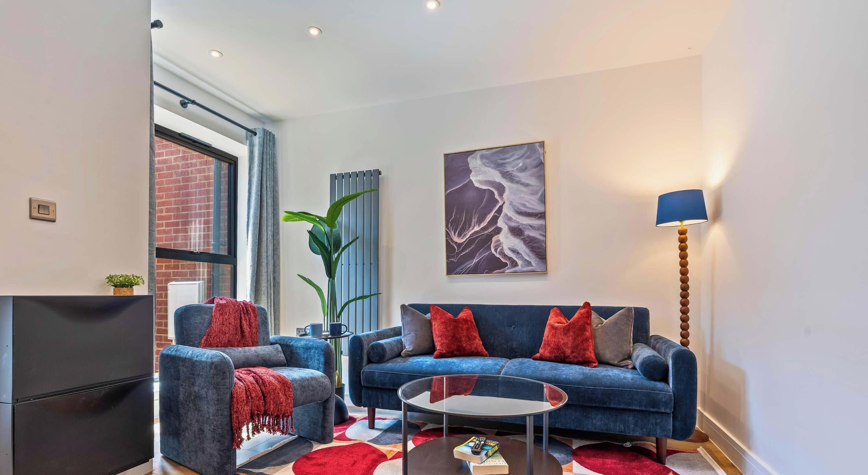 A modern living room with a blue sofa, a glass coffee table, and a large window.