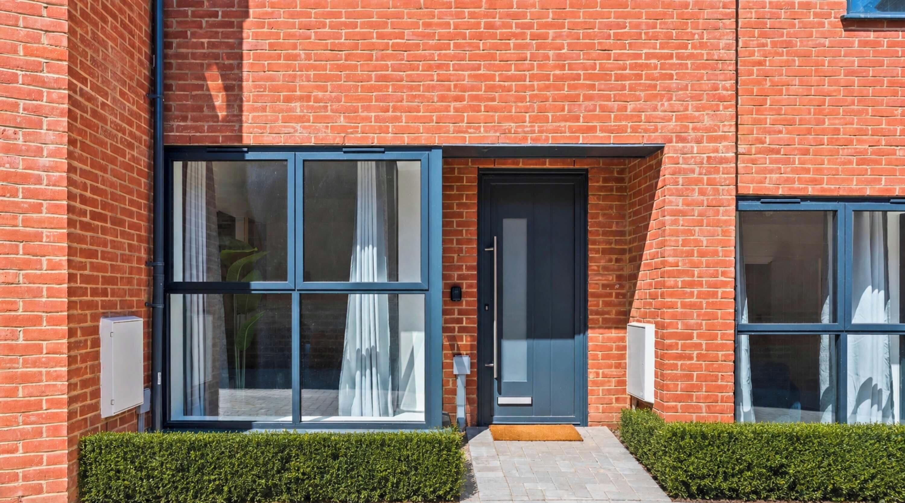 A modern building with a brick facade, large glass windows, and a dark-colored door.