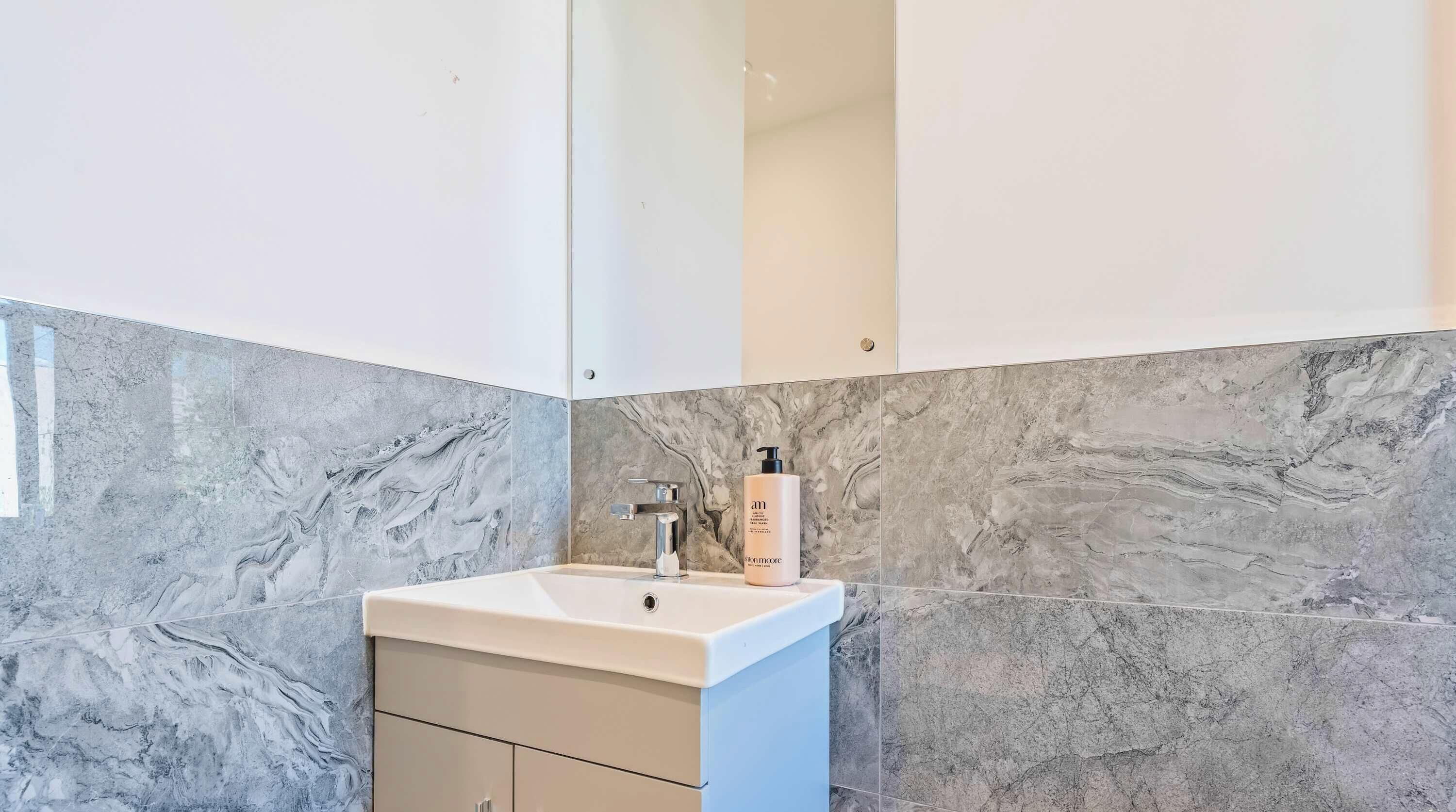 Un baño con lavamanos de mármol, un espejo y una botella de jabón para manos.