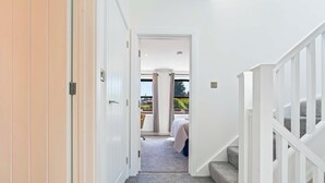 A hallway with a carpeted floor, white walls, and a staircase with a white railing. - Modern Reading House|Contractor & Family Friendly (Reading)