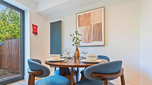A dining area with a round table, four chairs, a vase with greenery, and a framed abstract painting on the wall. - Modern Reading House|Contractor & Family Friendly (Reading)