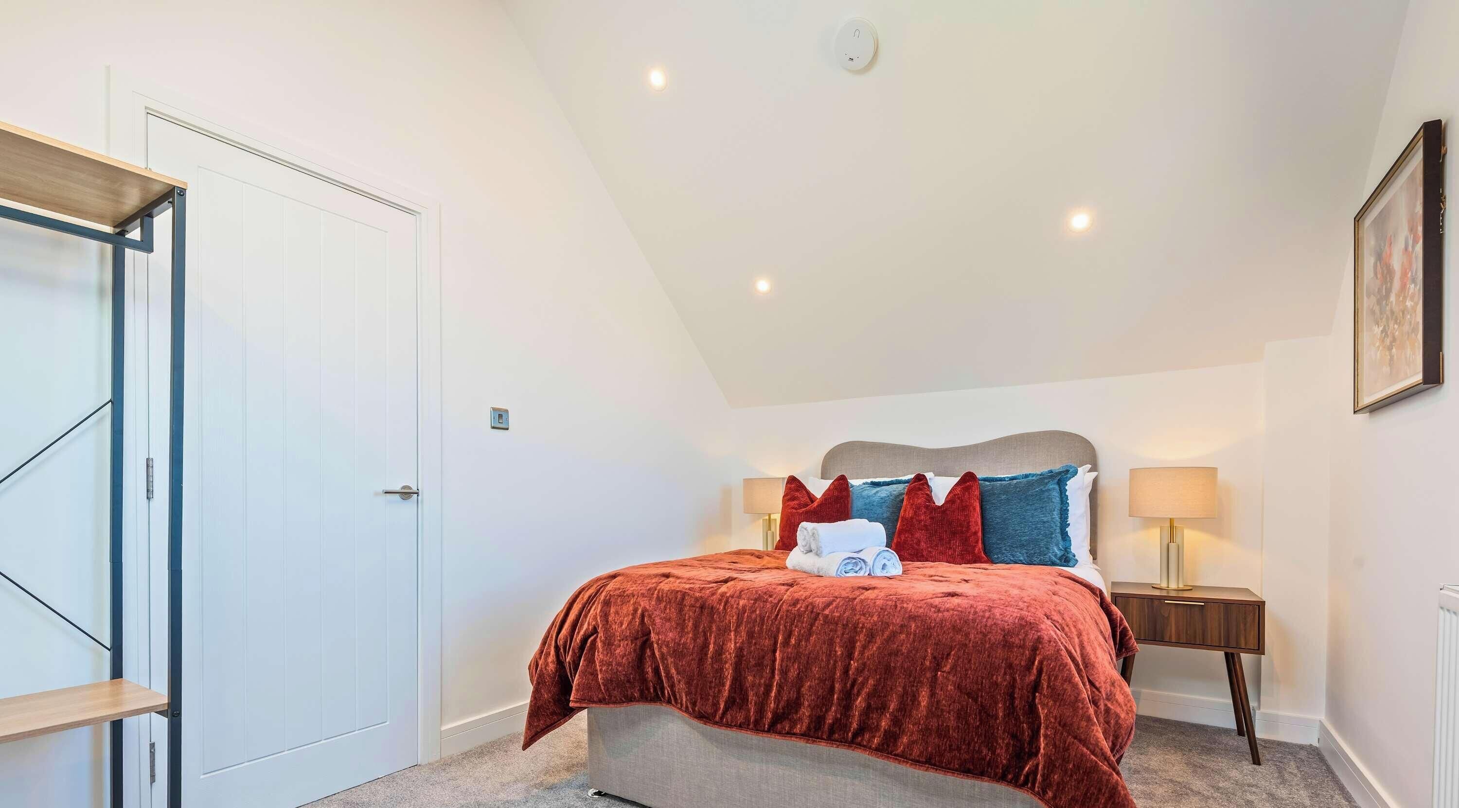 Un dormitorio con cama, mesitas de noche, una puerta y una lámpara en el techo.