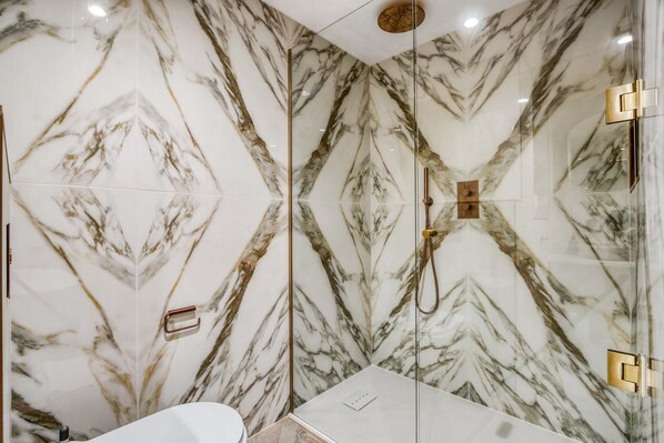 A bathroom with marble walls, a glass shower enclosure, and a white sink. - Goleudy Apartment - Two Bedroom Apartment, Sleeps 4 (The Mumbles)