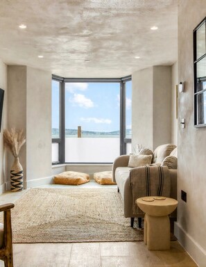 A modern living room with a large window, a sofa, a round coffee table, and a woven rug. - Goleudy Apartment - Two Bedroom Apartment, Sleeps 4 (The Mumbles)