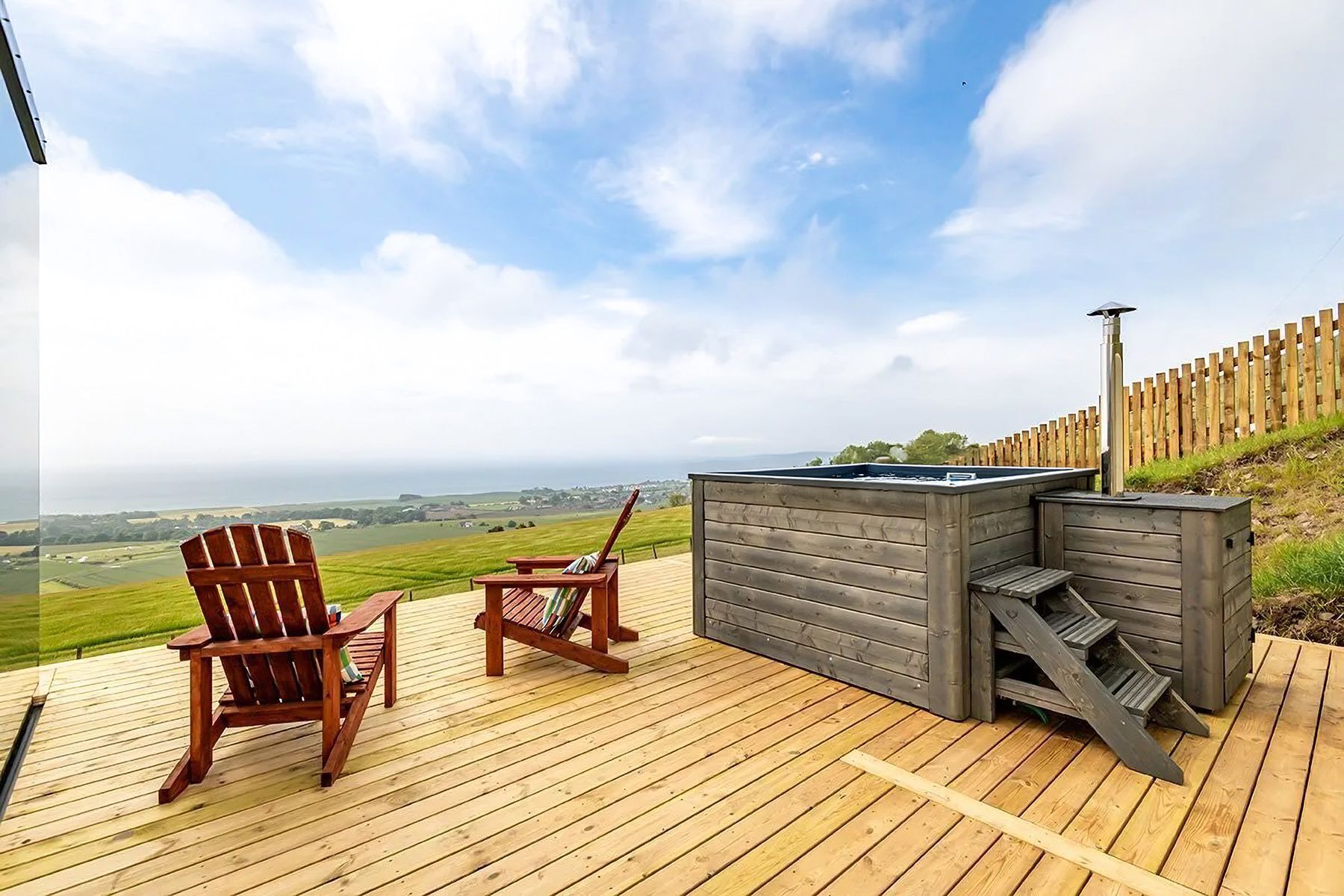 Eine Holzterrasse mit zwei Adirondack-Stühlen und einem Whirlpool.