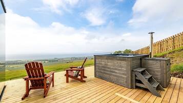 A wooden deck with two Adirondack chairs and a hot tub.