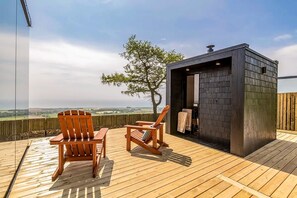 A wooden deck with two wooden chairs and a small wooden structure, possibly a sauna or hot tub, with a view of the countryside.