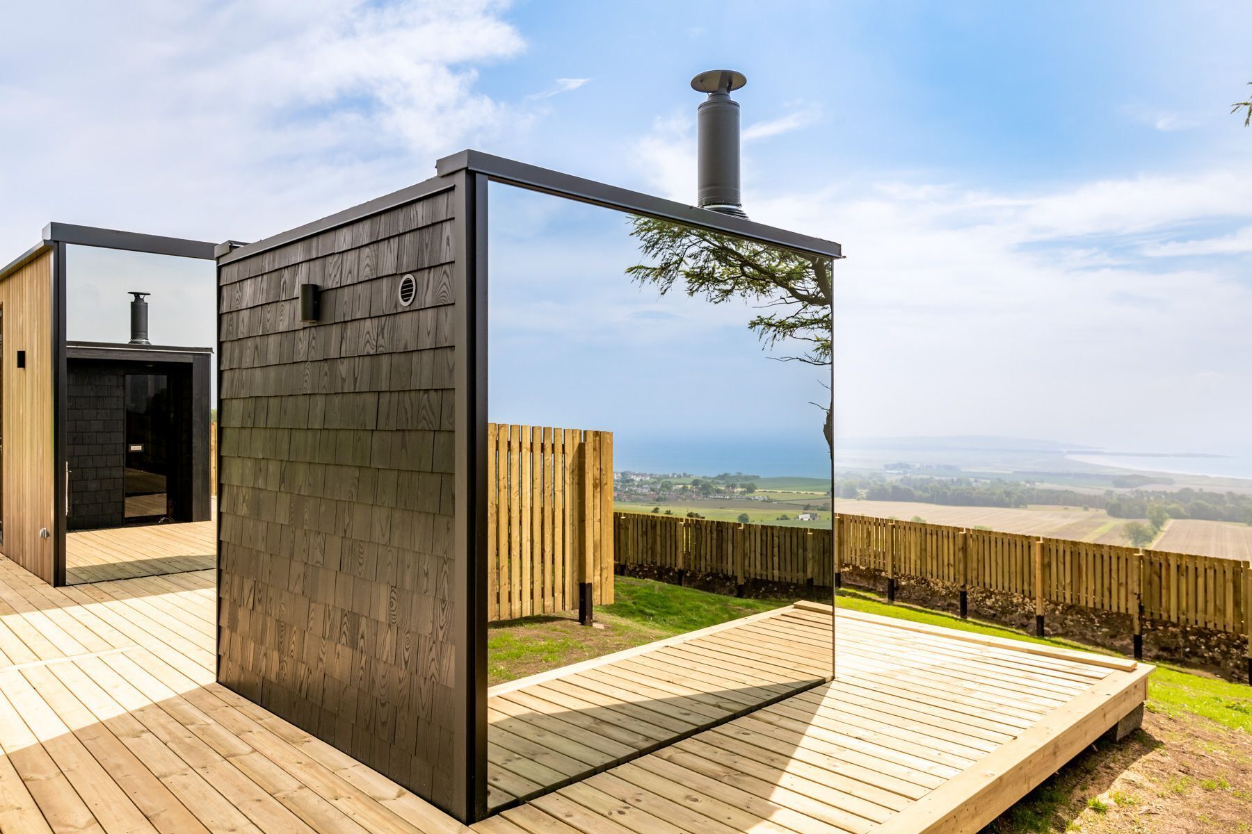 A modern outdoor deck with a wooden floor, a metal structure, and a view of the countryside.