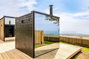 Una terraza moderna al aire libre con piso de madera, estructura metálica y vistas al campo.