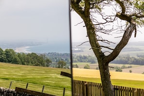 A view of a coastal landscape with a tree in the foreground and a distant view of the sea and wind turbines.