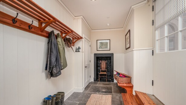 A hallway with a coat rack, boots, a wicker basket, and a chair by a fireplace.