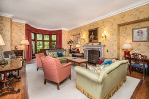 Een klassieke woonkamer met een open haard, bloemenbehang en antieke meubels.