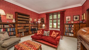 A room with a red sofa, a wooden chair, and a red ottoman. There are bookshelves filled with books and a fireplace.