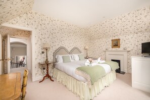 A bedroom with a checkered headboard, a bed with green and white bedding, a fireplace, and a television.