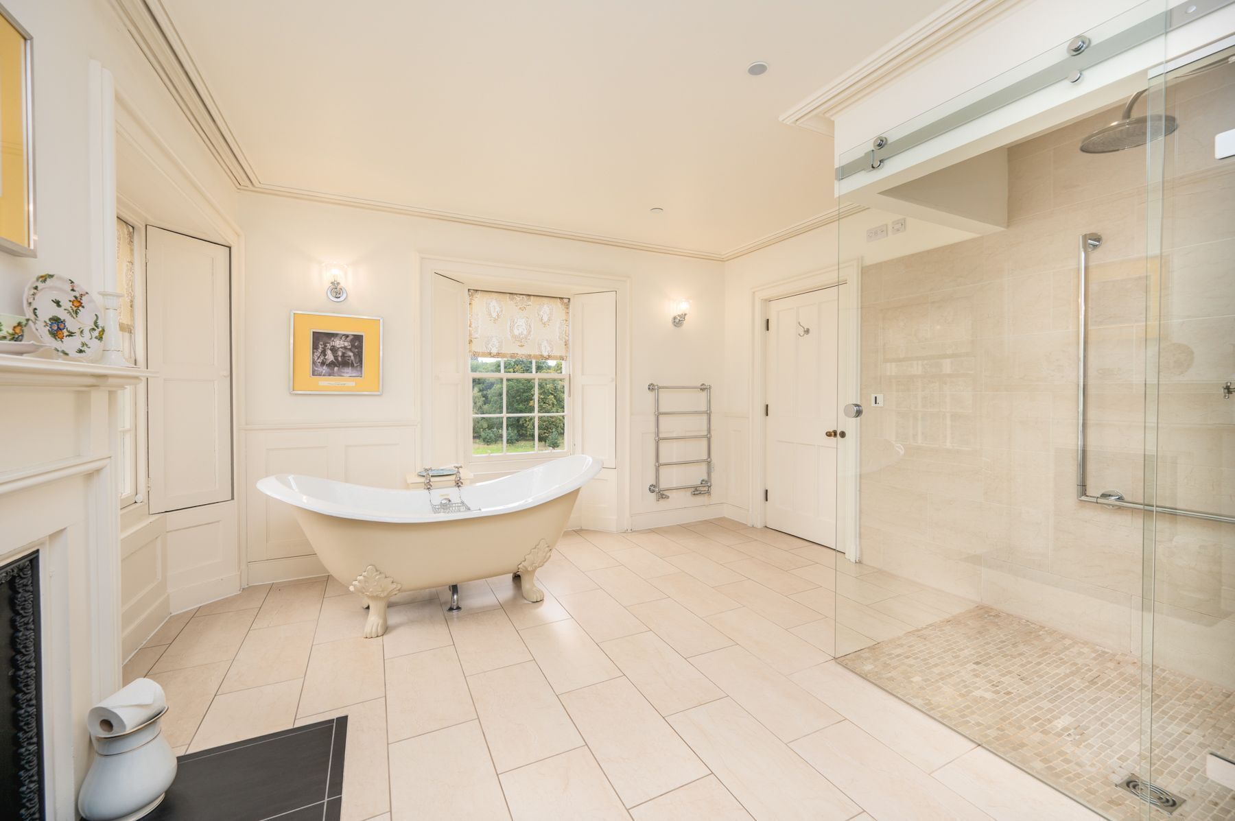 Une salle de bain spacieuse avec une baignoire sur pieds, une douche à l’italienne et une fenêtre donnant sur un paysage verdoyant.