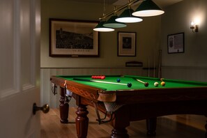 A pool table with balls and cues, a framed picture on the wall, and a billiard rack.