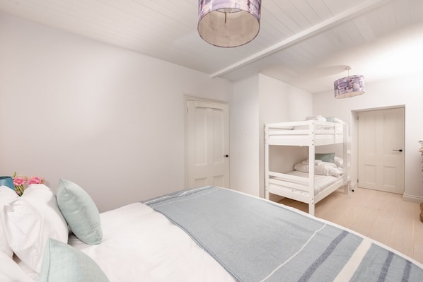 A bedroom with a bunk bed, a single bed, a bedside table, and a hanging light fixture.