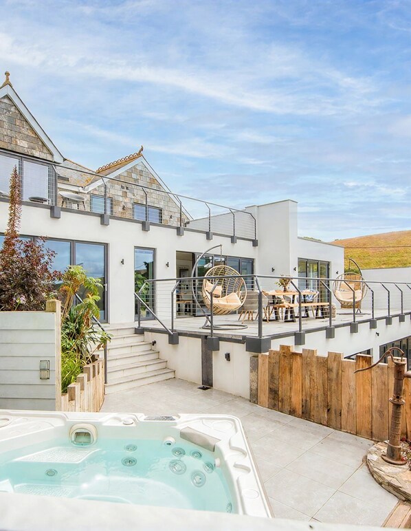A modern house with a hot tub, outdoor seating, and a staircase leading to a deck.