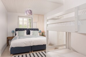 Een slaapkamer met een stapelbed, een nachtkastje met een lamp en een raam met jaloezieën.