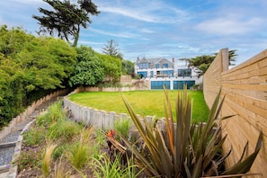 A landscaped garden with a wooden fence, a variety of plants, and a modern house with a large window and a balcony.