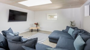 Una sala de estar moderna con un sofá modular, un televisor de pantalla plana, un banco de madera pequeño y un cuadro en la pared.