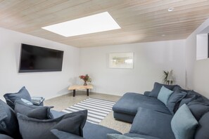 A modern living room with a sectional sofa, a flat-screen TV, a small wooden bench, and a framed picture on the wall.