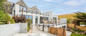 A modern two-story house with a balcony, outdoor seating, and a garden.