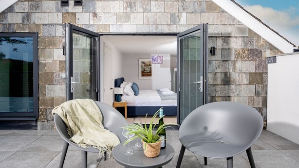 Una habitación moderna con fachada de piedra, una cama, una mesita con una planta y dos sillas.