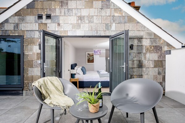 A modern room with a stone facade, a bed, a small table with a plant, and two chairs.