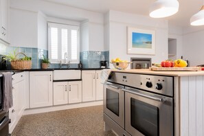 A modern kitchen with white cabinetry, stainless steel appliances, and a window with blinds.