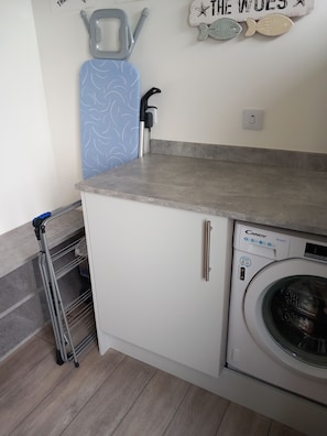 A kitchen with a built-in washing machine, a metal drying rack, and a wall-mounted towel rack.